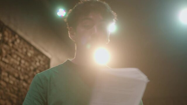 Young handsome actor reading script on paper, performing drama monologue and playing his role during rehearsal on theater stage