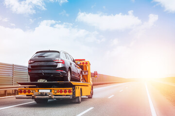 A tow truck on the public road. Tow truck with broken car on country road. Tow truck transporting car on the highway. Car service transportation concept. - obrazy, fototapety, plakaty