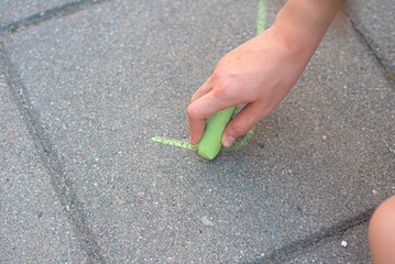 A girl's hand draws with chalk on a tratoir tile