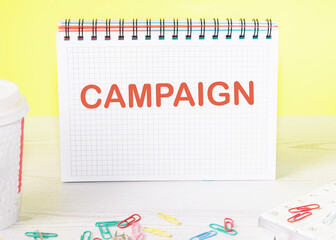 Campaign the word is written on a blank sheet in a notebook standing on a table on a yellow background