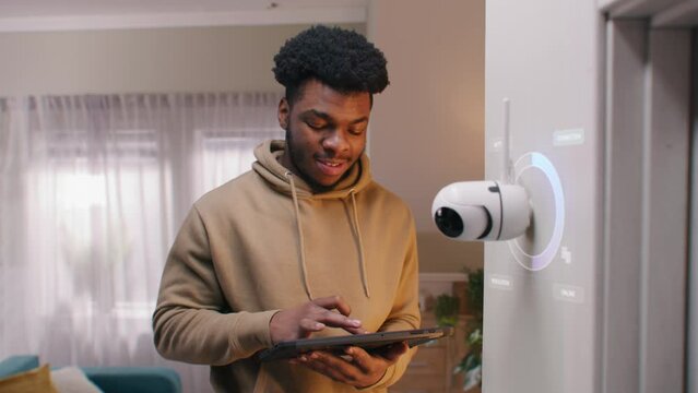 African American man sets up security camera with AI recognition at home using digital tablet. 3D circles render shows wireless internet connection with CCTV camera. VFX animation. Monitoring system.
