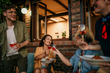 Group of smiling friends sitting and cheering with wine glasses together during a evening on the...