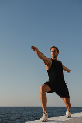 Obraz premium Confident young male athlete doing stretching exercises with the sea view on background