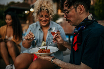 Loving couple sitting outdoors in house yard during an evening, and sharing a plate of pasta spaghetti.