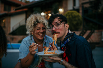 Loving couple sitting outdoors in house yard during an evening, and sharing a plate of pasta...