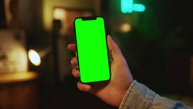Hands man holding and using mobile phone with a vertical green screen indoors. Social media. Mock up