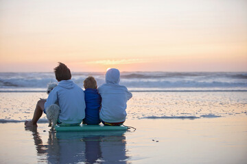 Happy children, boys, playing on the beach on sunset, kid cover in sand, smiling, laughing