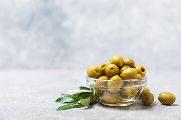 Green olives on a light marble background. Fresh juicy olives in a bowl and fresh olive leaves....
