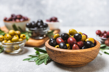 A set of green, red and black olives on a light marble background. Various types of olives in bowls and fresh olive leaves. Vegan. Olive fruits. Place for text. Copy space.