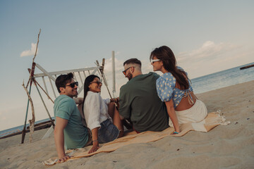 Fototapeta premium Four young friends talking and smiling while spending carefree time seaside