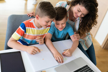 Caring supportive mother helping her sons finish their school chores in front of laptop.