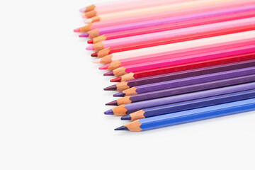 Multi-colored pencils lie on a white table, the violet range of colors
