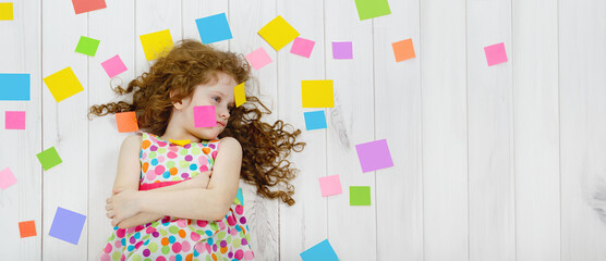 Thoughtful child girl with sticky notes on clothes, forehead and around with stress and upset face.