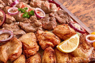 Part of the wooden board with fried meat and vegetables on the wooden table,close-up, shallow depth of field. Chicken meat and lemon in focus