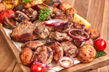 Part of the wooden board with fried meat and vegetables on the wooden table, close-up, shallow depth of field. Beef meat, champignons and onion in focus