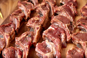 Part of the wooden board with metal skewers with raw uncooked lamb ribs meat for frying. Close-up perspective view, shallow depth of field. Meat, garlic and spices in focus