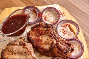 Part of the wooden board with fried beef meat with red onion rings, sauce and pita bread on the wooden table, close-up perspective view, shallow depth of field. Meat in focus