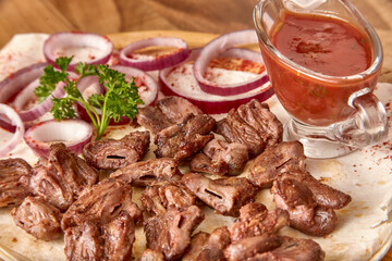 Part of the wooden board with fried beef meat with red onion rings, sauce and pita bread on the wooden table, close-up perspective view, shallow depth of field. Meat and sauce in focus