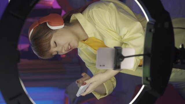 Beautiful girl in casual clothing with headphones and smartphone, talking in front of the camera at home studio. Vertical video HDR BT2020 HLG Material.