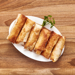 White plate with fried pita rolls with meat on the wooden table with parsley near it. Top view, flat lay