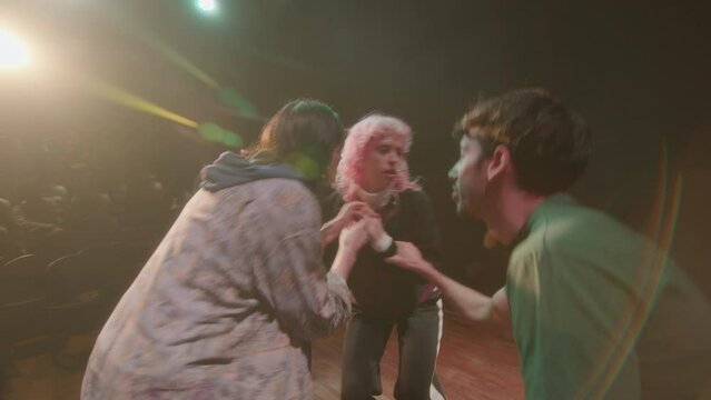 Group of young emotional performers playing drama on stage of modern theater during rehearsal, director watching their act