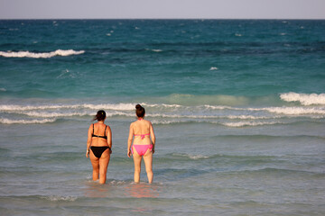 Two women in swimwear going to swim in sea water. Vacation on tourist resort