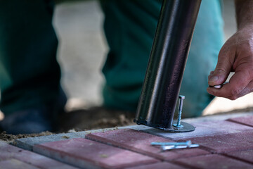 The maintenance man knelt down and bolted the leg from the park bench to the paving stones.