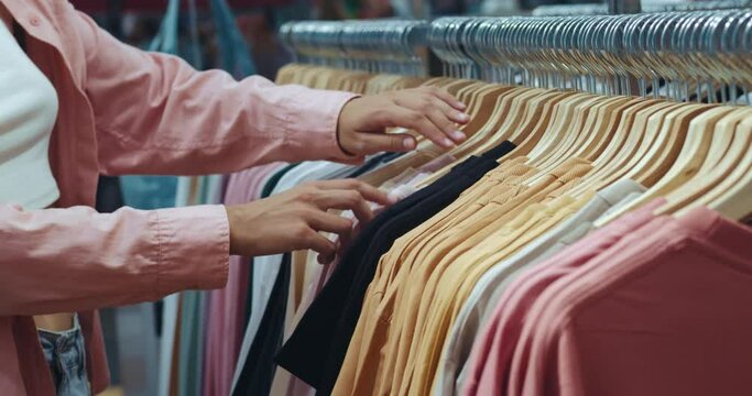 Close-up of female hands plucked hanger choosing clothing store. Unrecognizable woman hand runs across a rack of clothes buying clothes in a shopping mall. Sale promotion and clothing store concept.