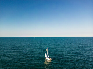 aerial view of a sailboat plowing alone in slightly rough seas. The photo conveys a sense of serenity and tranquility without forgetting the danger of the sea