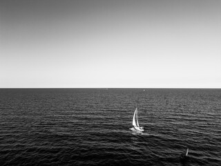 aerial view of a sailboat plowing alone in slightly rough seas. The photo conveys a sense of serenity and tranquility without forgetting the danger of the sea