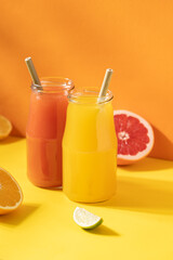 Grapefruit and orange juice in bottles on colorful yellow and orange background with copy space. Detox, vitamin cocktail in bottles