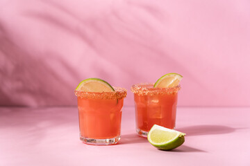 Grapefruit tropical cocktail with lime and ice on pink background. Refreshing summer drinks