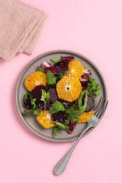 Seasonal vitamin salad orange beetroot and arugula in plate on pink background. Diet, healthy eating concept