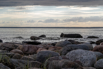 Sunset view from parispea beach in Lahemaa national park, Estonia. Image shows sunset with partial clouds and a calm sea washing over the rocky beach. August 2023