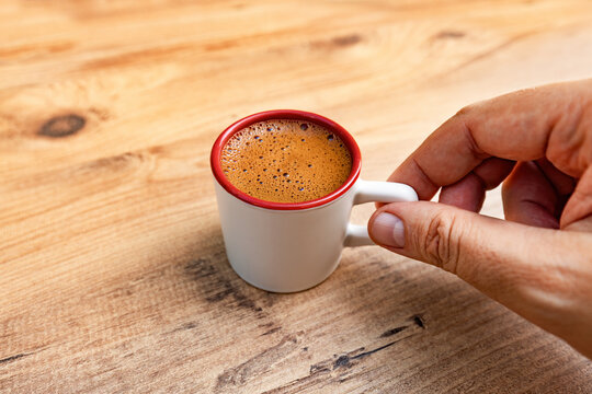 A man holding a cup of hot Turkish coffee standing on wooden table.  Black coffee. Warm, strong drink