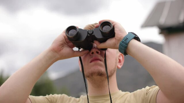 The young man is scrutinizing something through binoculars.