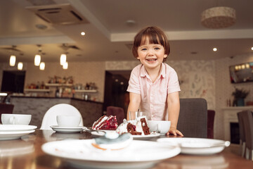 a little boy, at the table at home or in a cafe, restaurant, on a holiday, celebrates his birthday, there is a plate with a cake on the table