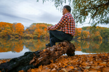 a man sits on a log by the river bank and enjoys the scenery, beautiful nature in the autumn...