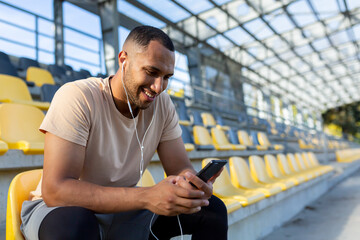 Happy and satisfied man after jogging and fitness class sitting and using smartphone, African...