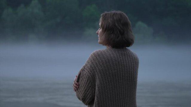 A woman in a sweater on the bank of a foggy river in the evening. Natural sound