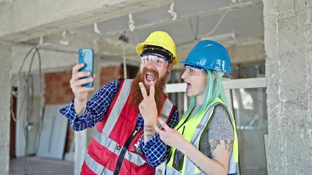Man and woman builders smiling confident make selfie by smartphone at construction site