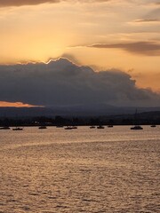 The rays of the sun break out from behind a threatening cloud and illuminate the bay with yachts at sunset in Syracuse.