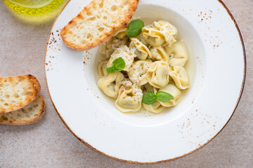 Tortellini in bouillon served with grated parmesan cheese and ciabatta in a beige plate, middle close-up, top view