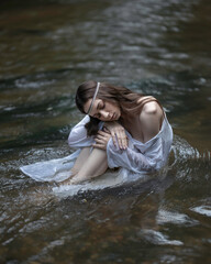 A girl in a Slavic white shirt sits in flowing water