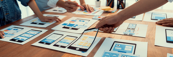 Panorama shot of front-end developer team brainstorming UI and UX designs for mobile app on paper...