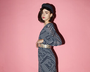 young fashion woman in black and white contrast dress and vintage cap on pink background