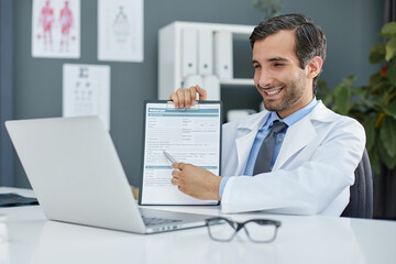 Close up of a doctor and patient hands while phisician pointing into medical history form at clipboard