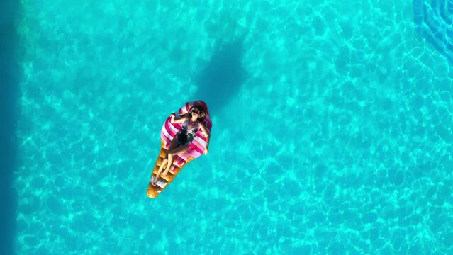 Sexy woman rest and sunbath on a float in the pool, top view aerial shot. Young woman in a bikini swimsuit floating on an inflatable pink mattress top view