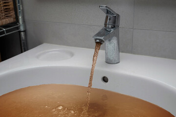 Dirty brown tap water after floods in the city streets after heavy rain. Severe weather disaster.
