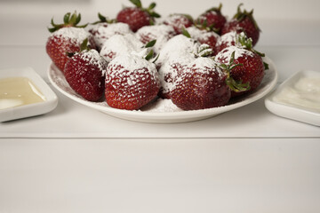 Beautiful juicy ripe red strawberries sprinkled with powdered sugar on a white round plate in the center of the frame on a white background. Close-up. - Powered by Adobe